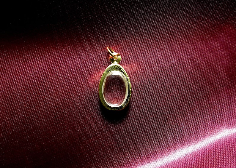 K&ouml;nnte beinhalten: Ein ovaler Anh&auml;nger aus Gold mit einem klaren Glaseinsatz. Der Anh&auml;nger liegt auf einem roten Samt-Hintergrund.