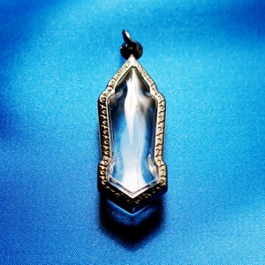 Może przedstawiać: Srebrny wisiorek z przezroczystym kryształem w środku. Wisiorek ma kształt spiczastego owalu i ozdobną ramkę.