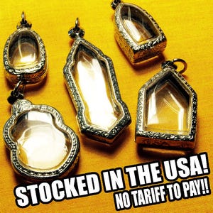 May include: Five silver-toned pendants with clear glass inserts are displayed on a yellow background. The pendants have various shapes, including oval, rectangular, and house-like designs. Each pendant has a loop for hanging.