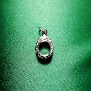 Peut inclure: Un pendentif en argent avec un cadre ovale orné. Le pendentif est sur un fond vert.