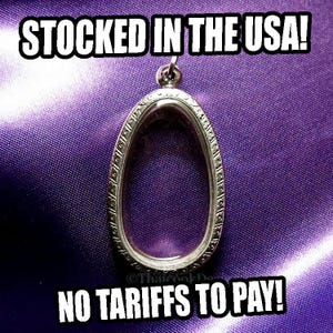 May include: A silver-colored oval pendant with a decorative border, hanging against a purple satin background. The text "STOCKED IN THE USA!" and "NO TARIFFS TO PAY!" are displayed in white block letters.