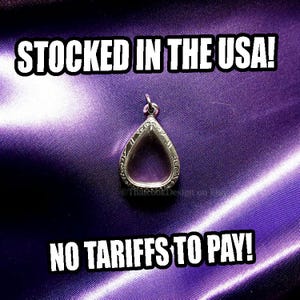 May include: A silver-colored, teardrop-shaped pendant with an ornate border, displayed on a purple satin fabric. The text "STOCKED IN THE USA!" and "NO TARIFFS TO PAY!" are in white block letters.