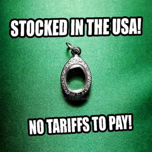 May include: A silver-colored pendant setting with an oval-shaped bezel, featuring ornate scrollwork around the edges. The pendant hangs from a small loop. The text "STOCKED IN THE USA!" and "NO TARIFFS TO PAY!" are displayed in white block letters on a green background.