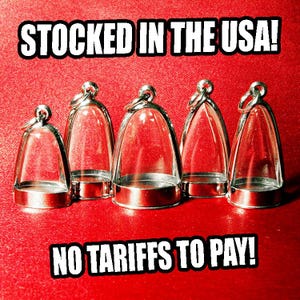 May include: Five clear glass bell-shaped pendants with silver-colored metal bases and loops. The pendants are arranged on a red textured surface. Text at the top reads "STOCKED IN THE USA!" and at the bottom, "NO TARIFFS TO PAY!"