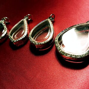 Può includere: Tre ciondoli d'argento a forma di lacrima con inserti in vetro trasparente. I ciondoli sono su uno sfondo rosso.