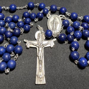 May include: A blue rosary with a silver crucifix and a silver medal of the Virgin Mary. The beads are made of lapis lazuli.
