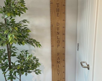 May include: A wooden height chart with engraved measurements and the text "THE DUNLOP FAMILY RULE". The chart is made of light-colored wood and is mounted on a white wall. The measurements are in feet and inches.