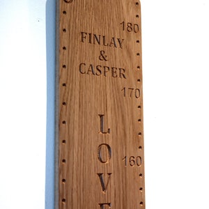 Peut inclure: Une toise verticale en bois brun clair aux coins arrondis, grav&eacute;e avec le texte FINLAY & CASPER et LOVED. La planche pr&eacute;sente des marquages imp&eacute;riaux pour 5 et 6 pieds, ainsi que des mesures m&eacute;triques allant de 150 &agrave; 180 centim&egrave;tres.