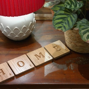 Peut inclure: Des tuiles en bois orthographiant le mot "HOME" sur une table en bois. Les tuiles sont numérotées de 1 à 4. Un abat-jour rouge et une plante en pot sont en arrière-plan.