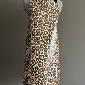 May include: A brown and white leopard print apron with adjustable straps. The apron is made of a waterproof material and has a large pocket on the front.