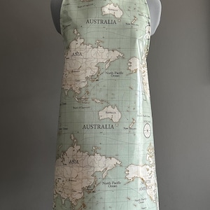 May include: A light green apron featuring a world map design. The map includes continents like Australia, Asia, and North America, with ocean names. The apron has a neck strap and waist ties, offering coverage for cooking or crafting.