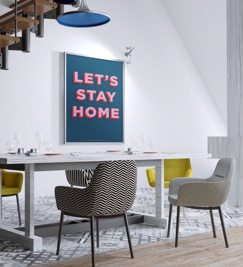 Puede incluir: Un comedor con una mesa blanca y cuatro sillas. Las sillas est&aacute;n tapizadas con diferentes telas, incluyendo un patr&oacute;n de chevron blanco y negro y una tela gris. Un p&oacute;ster enmarcado con el texto "Let's Stay Home" cuelga de la pared.