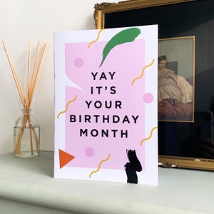 Puede incluir: Una tarjeta rosa y blanca con el texto "Yay it's your birthday month" en negro. La tarjeta tiene un diseño abstracto verde, negro y naranja.