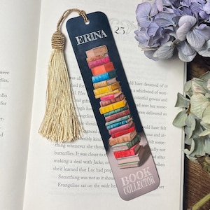 May include: A navy blue bookmark featuring a stack of colourful books and the text "ERINA" and "BOOK COLLECTOR". It has a gold tassel. The number 25 is also visible on the bookmark.