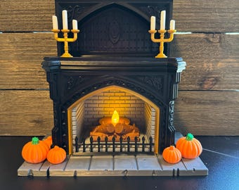 May include: A black decorative fireplace with a lit faux fire and two gold candle holders. The fireplace is decorated with orange pumpkins. The fireplace is a Halloween or fall-themed decoration.