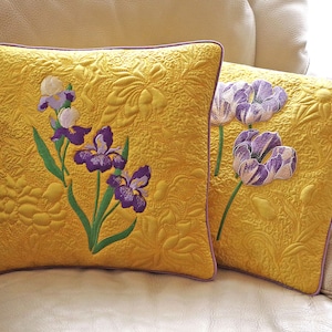 Peut inclure: Deux coussins jaunes avec des motifs floraux brodés. Un coussin présente des iris violets et blancs, tandis que l'autre présente des tulipes violettes.