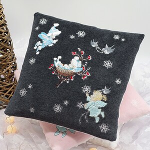 May include: A dark gray pillow with embroidered winter scenes. The pillow features a bird, a nest with baby birds, and a snowflake design. The pillow is made of a soft, plush fabric.