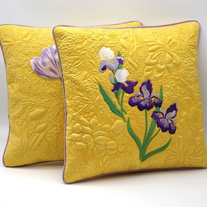 May include: Two yellow throw pillows with embroidered purple and white iris flowers. The pillows have a light purple trim.