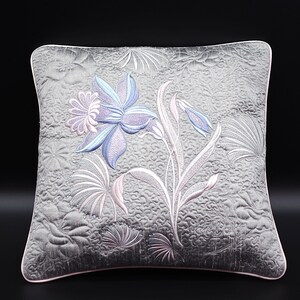 Puede incluir: Una almohada decorativa gris y rosa con un diseño floral bordado. Las flores son azules, moradas y rosas. La almohada está acolchada y tiene una sensación suave y lujosa.