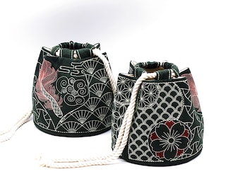 May include: Two green drawstring bags with white rope handles. The bags are decorated with white embroidery of Japanese-inspired patterns. One bag features a red fish design, while the other has a red flower design.