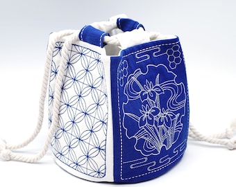 May include: A blue and white drawstring bag with a geometric pattern on one side and a floral design on the other side. The bag is made of fabric and has a white drawstring.