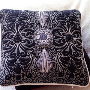 Puede incluir: Una almohada decorativa en blanco y negro con un intrincado diseño floral. La almohada está acolchada con un patrón en relieve y tiene un borde blanco.