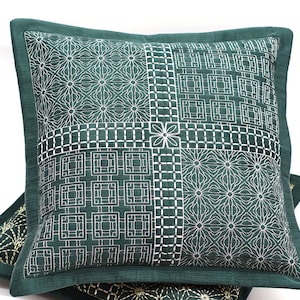 Puede incluir: Una almohada verde con un patrón geométrico blanco. La almohada está hecha de una tela suave y texturizada.