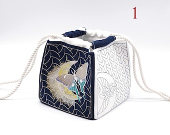 May include: A blue and white drawstring bag with a butterfly and moon embroidery design. The bag has a white rope handle.