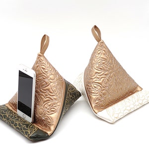 May include: Two quilted phone stands, one in gold and white and one in gold and green. The gold and green stand has a phone in it.
