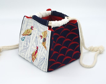 May include: A white and blue fabric drawstring bag with a red and blue geometric pattern on one side and a white and blue floral pattern with embroidered birds on the other side. The bag has a white rope handle.