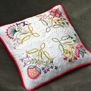 Peut inclure: Un oreiller blanc avec une bordure rouge et des motifs floraux brodés dans des tons de rose, vert, jaune, orange et violet.