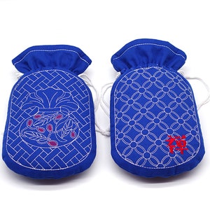 Op de afbeelding: Twee blauwe stoffen zakjes met witte borduursels. Eén zakje heeft een bloemenmotief en het andere een herhalend cirkelpatroon. Beide zakjes hebben witte trekkoorden.