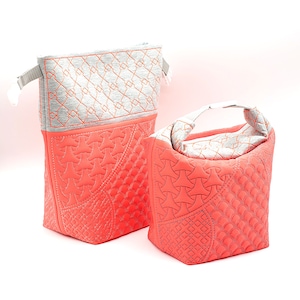 Könnte beinhalten: Zwei gesteppte Stofftaschen mit orangefarbenen Nähten. Die größere Tasche ist grau mit einem geometrischen Muster und die kleinere Tasche ist korallenfarben mit einem geometrischen Muster. Beide Taschen haben einen Griff.