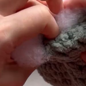 May include: A close-up of a hand holding a multi-colored knitted hat. The hat is made of soft, fluffy yarn in shades of pink, green, and gray.