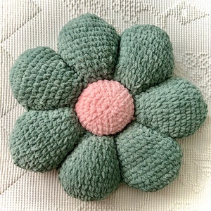 May include: A green and pink flower-shaped pillow with a textured fabric. The pillow is made of multiple fabric pieces sewn together to form a flower shape.