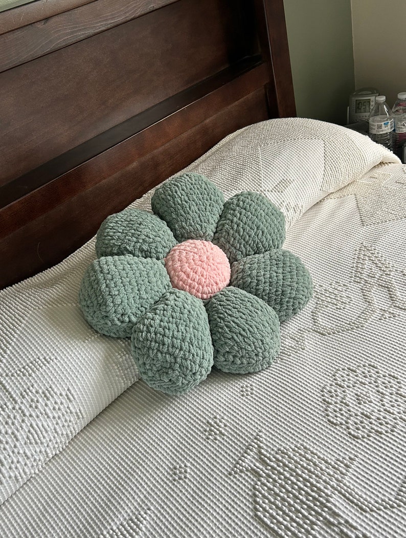May include: A green and pink crocheted flower-shaped pillow on a white bed.
