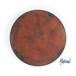 May include: A circular, flat object with a textured, mottled surface in shades of deep orange, rust, and dark brown. The surface features a weathered, oxidized appearance with darker patches throughout. The word Natural is written in script.