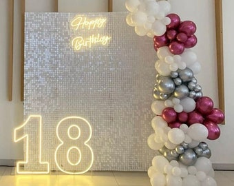 Könnte beinhalten: Geburtstagsdekoration mit einer Paillettenwand, einem Neon-Schriftzug "Happy Birthday" und der Neon-Zahl "18". Ein Ballonbogen in Weiß, Silber und Burgunderrot verleiht der Feier eine festliche Note.
