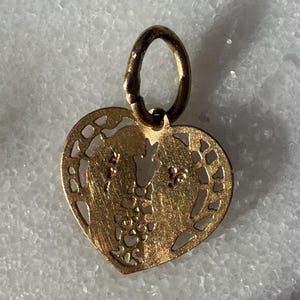 Puede incluir: Un colgante de coraz&oacute;n de oro con un delicado dise&ntilde;o de corte. El colgante presenta dos figuras abraz&aacute;ndose dentro del coraz&oacute;n.