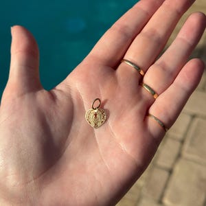 Puede incluir: Un dije de coraz&oacute;n de oro con intrincados detalles de filigrana. El dije cuelga de un peque&ntilde;o lazo de oro.