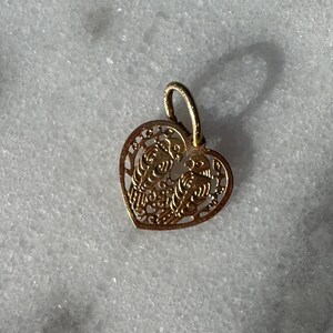 Puede incluir: Un colgante de coraz&oacute;n de oro con un delicado dise&ntilde;o de filigrana. El colgante presenta dos figuras entrelazadas dentro del coraz&oacute;n.