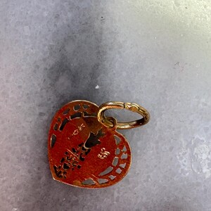 Puede incluir: Un amuleto de coraz&oacute;n de oro con intrincados recortes y un peque&ntilde;o anillo adjunto. El amuleto tiene el n&uacute;mero "585" estampado en &eacute;l.