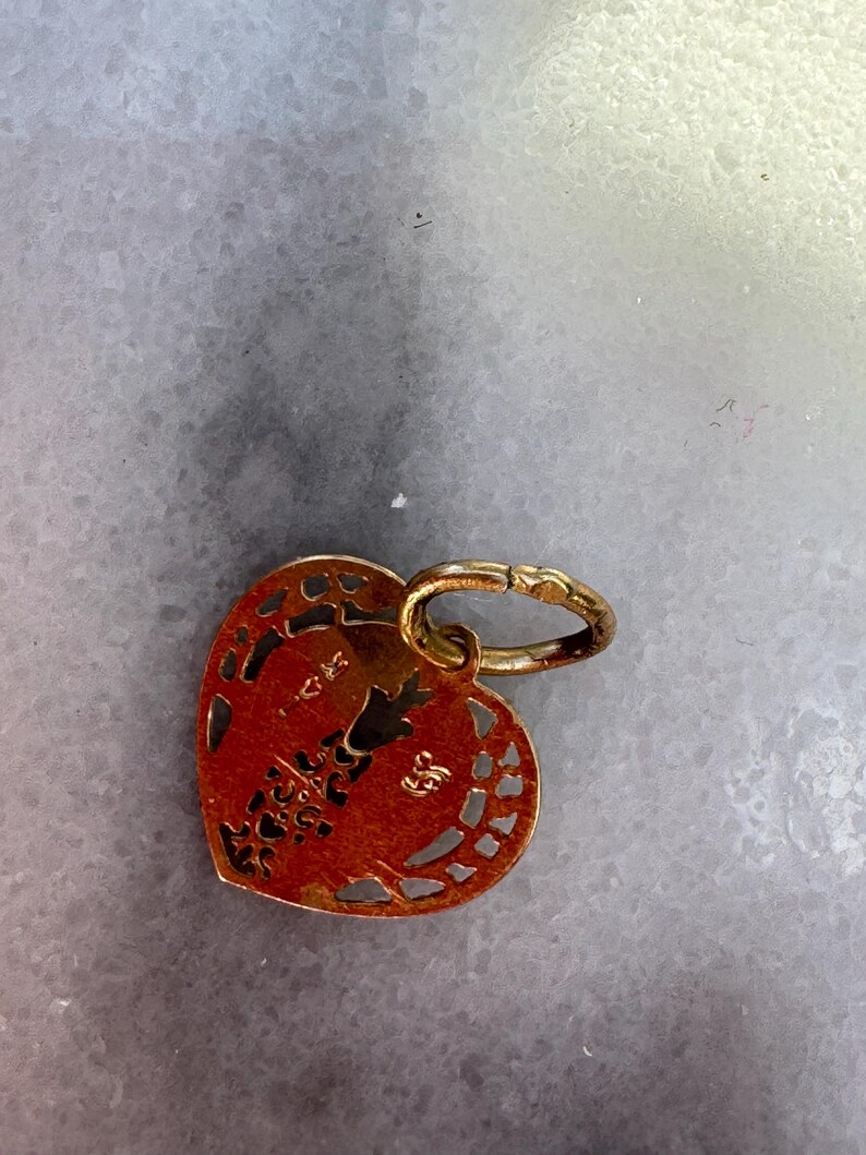 Puede incluir: Un amuleto de coraz&oacute;n de oro con intrincados recortes y un peque&ntilde;o anillo adjunto. El amuleto tiene el n&uacute;mero "585" estampado en &eacute;l.