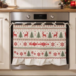 May include: A cream-coloured oven towel featuring a festive pattern of red reindeer, green pine trees, and red snowflakes. The towel includes the red cursive text Baked with love and is attached to the oven handle with white fabric ties.