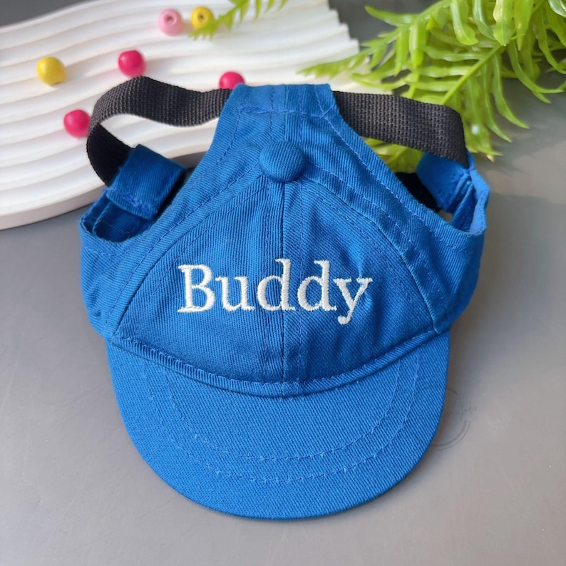 Peut inclure: Casquette de baseball bleue pour chien, avec le mot "Buddy" brod&eacute; en blanc. La casquette a une sangle noire et des trous pour les oreilles. Fabriqu&eacute;e en tissu doux.