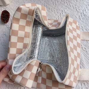 May include: Open insulated lunch bag with a beige and white checkered pattern. The interior is lined with a silver, reflective material. The bag has a zipper closure and a beige handle.