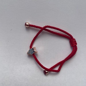 Puede incluir: Pulsera roja ajustable con un pequeño dije en forma de búho con piedras azules y transparentes. La pulsera tiene un pequeño dije de corazón y una cuenta de oro rosa.