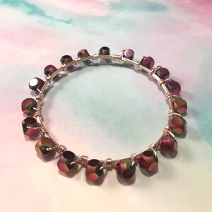 May include: A handcrafted bracelet with iridescent, multi-faceted beads in purple, green, and gold. The beads are strung on silver-coloured wire, creating a delicate piece of jewellery. This bracelet is a stylish accessory, perfect for adding a touch of colour.