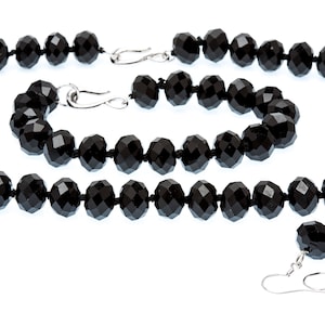 Puede incluir: Un conjunto de joyas de cuentas negras facetadas, que incluye un collar, una pulsera y pendientes. El collar y la pulsera tienen cierres plateados. Los pendientes tienen ganchos plateados. Las cuentas están ensartadas en un cordón negro.