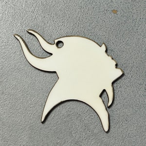 May include: A white, stylized elephant-shaped pendant with a gold-colored outline and a small hole at the top. The pendant has a smooth, glossy finish and is set against a gray background.